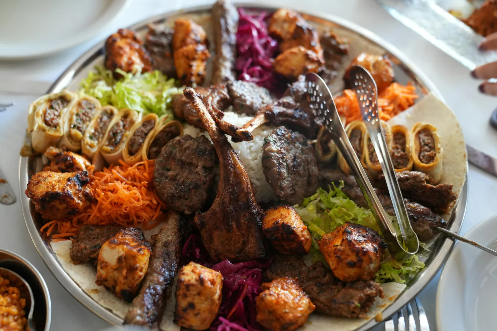 A large sharing platter of grilled meats and wraps, with serving tongs