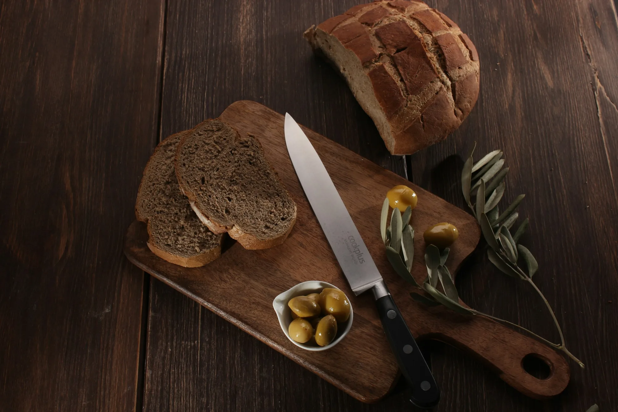 Bread, olives and an olive branch on a dark wooden board