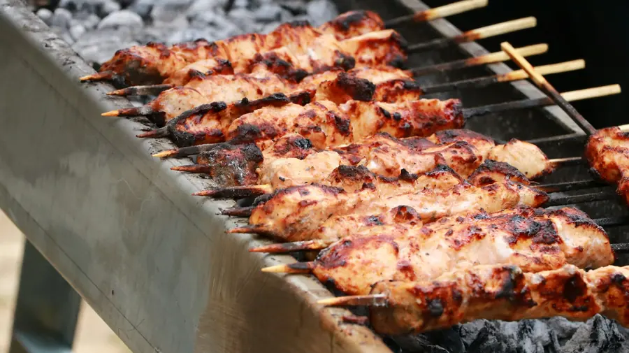 Marinated chicken kebab skewers cooking over a charcoal grill