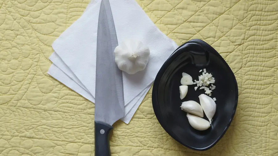 Fresh garlic cloves beside a bowl of whipped garlic sauce