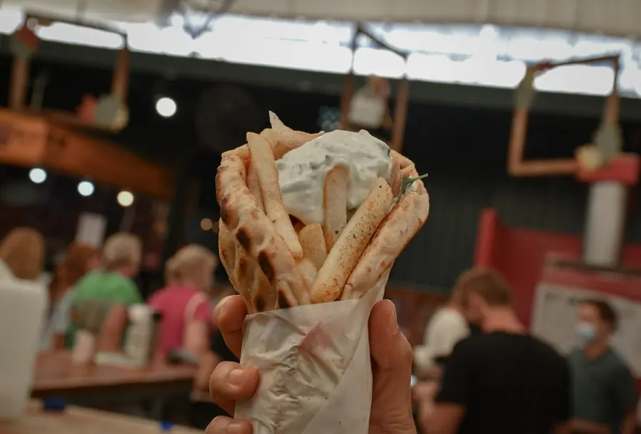 A gyro wrapped in pita with tomato, onion and white sauce