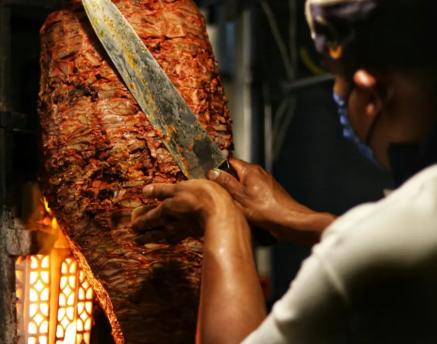 Meat being carved from a vertical spit with a long knife